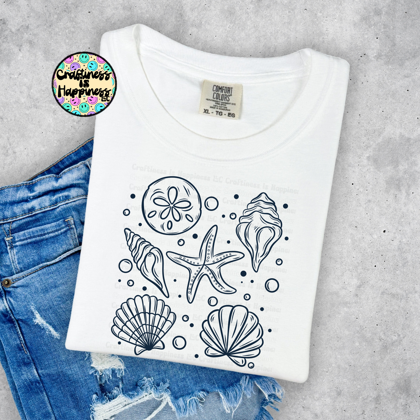 White t-shirt with black sea-themed designs on a concrete surface with jeans.