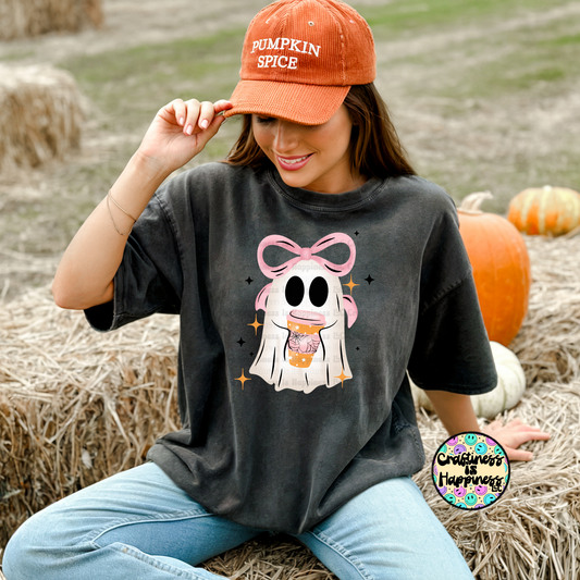 Woman wearing a black t-shirt with a ghost design and an orange 'Pumpkin Spice' cap, sitting in a pumpkin patch.