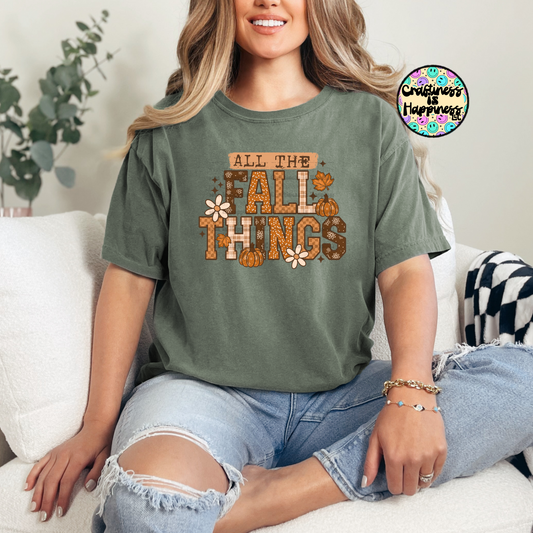 Woman wearing a green t-shirt with 'All the Fall Things' text, sitting on a couch.