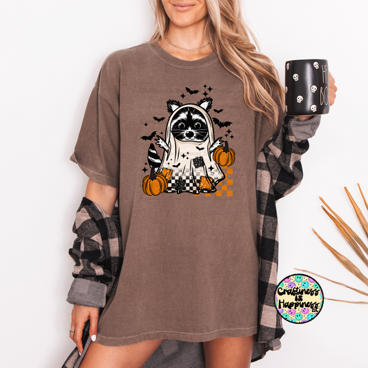 Person wearing a brown t-shirt with a Halloween-themed raccoon design, holding a mug.