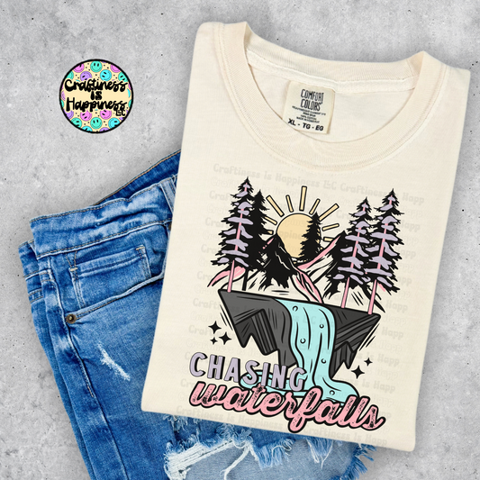 T-shirt with nature graphic and 'Chasing Waterfalls' text on a gray surface with jeans.