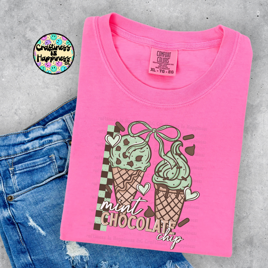 Pink t-shirt with mint chocolate chip ice cream design on a gray surface with jeans.