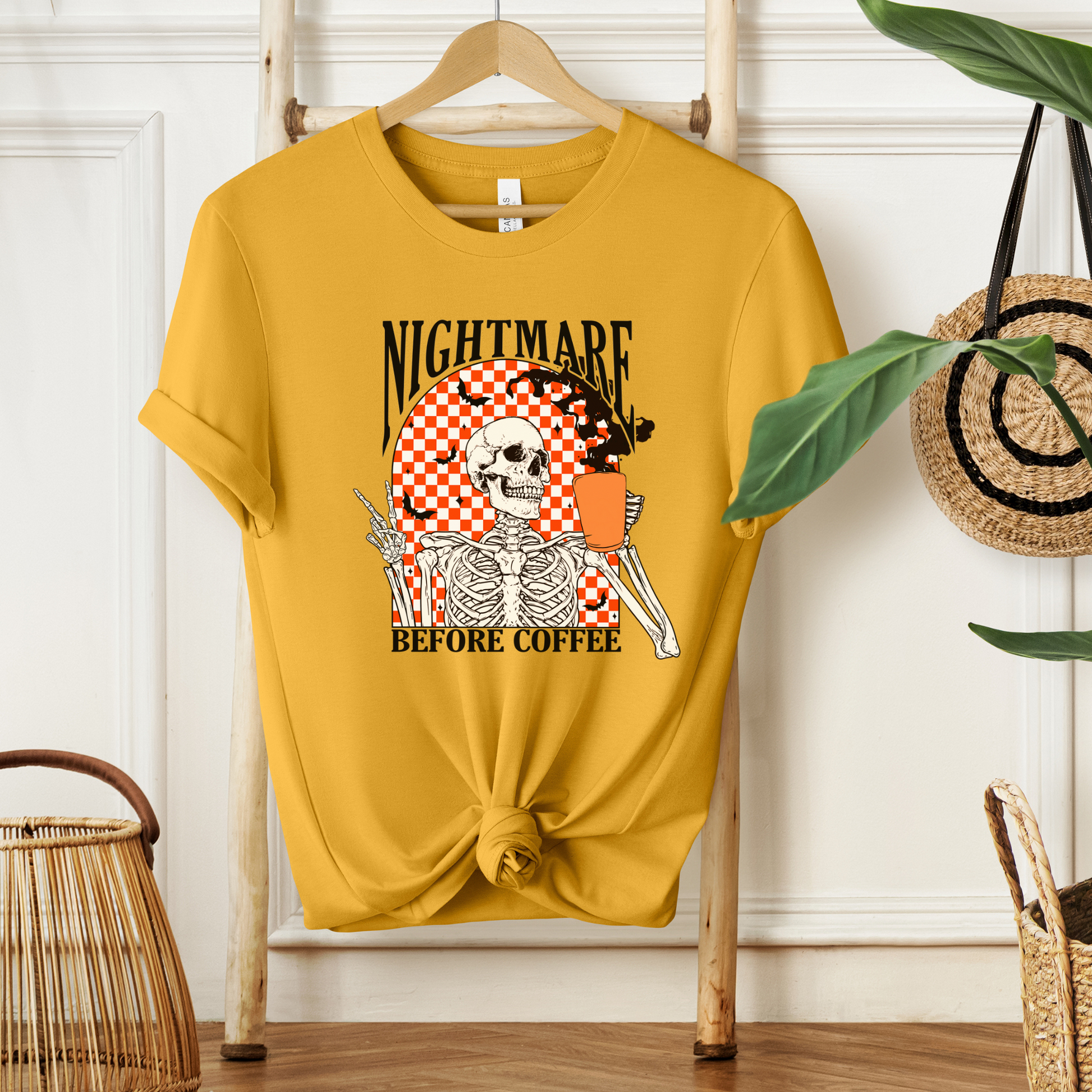 Mustard short sleeve shirt " Nightmare Before Coffee" saying,  retro orange & white checkerboard background with a skeleton holding a cup of coffee-front