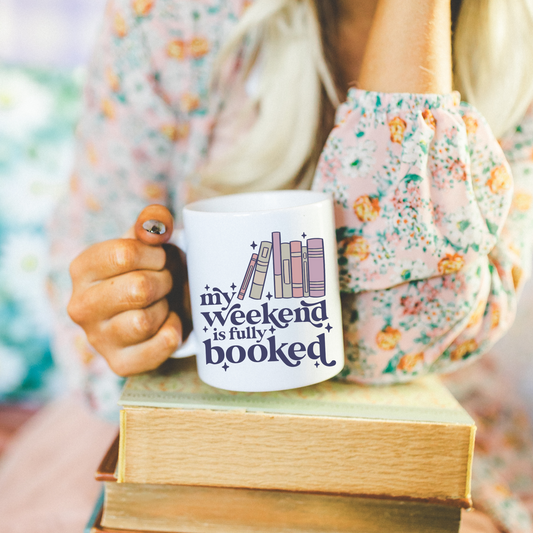 white 15oz mug "My Weekend is fully booked" with a stack of books and stars